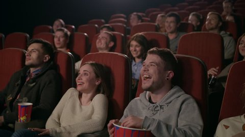 Young people laugh at comedy movie in cinema theatre. Young people laughing at cinema watching amusing comedy. Cheerful people watching comedy film in slow motion