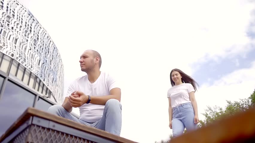 Man sitting on the stairs of a building and his woman coming from behing to him.