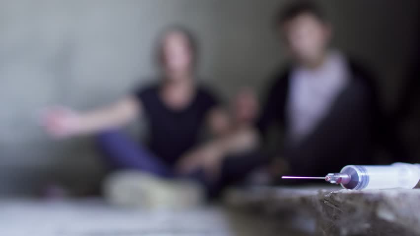 Two people sitting at the floor at the background of used syringe