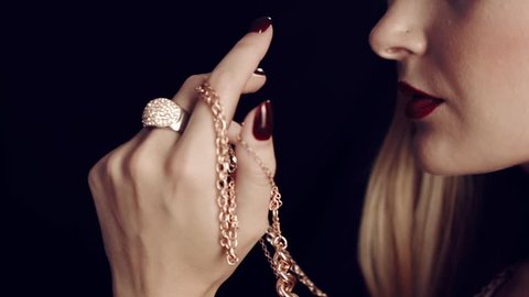 Close-up of  girl's hand with red nails holding gold chain. Jewelry for women. In the studio on a black background. Large gold ring with diamonds on finger.
