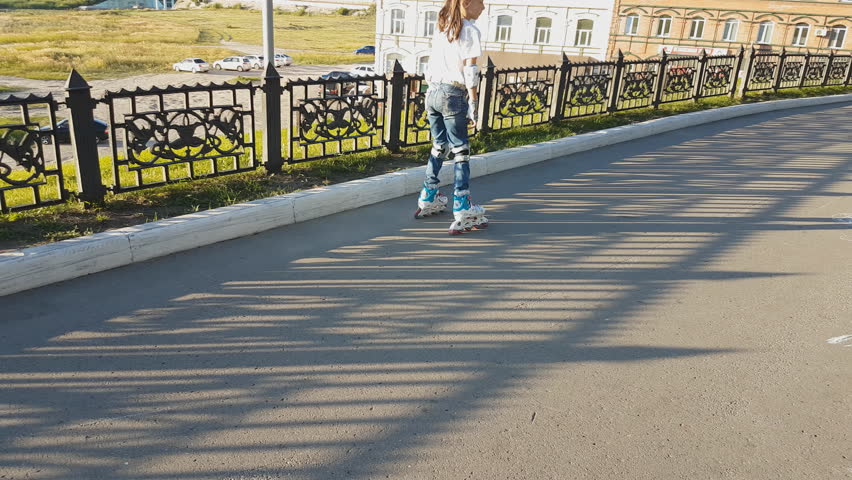 two sisters walk in the Park in summer. older sister on roller skates, younger sister runs after her with candy on a stick in her hand. happy childhood