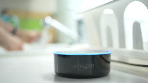 MONTREAL, CANADA - August 2018 : Smart home assistant device being used with voice commande in a kitchen while in the background somebody is washing dishes. Amazon Echo Alexa