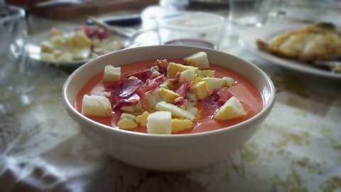 spreading olive oil on salmorejo cordobes, a typical spanish tomato soup similar to the gazpacho, topped with serrano ham, chopped boiled egg and croutons, on a set table