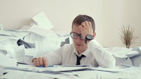Young businessman hid behind with stack papers. a huge pile of papers scattered on the table. paper work young man with glasses.