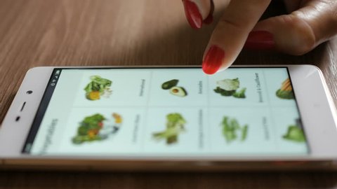 Woman orders food home in an online store using a smartphone. Female selects the vegetables in the grocery online store. Close-up. 4K UHD. Screen is blurred
