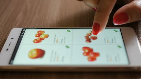 Woman orders food home in an online store using a smartphone. Female selects the fruit apples in the grocery online store.  Close-up. 4K UHD. Screen is blurred