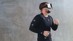 portrait of cheerful young man have fun dance while getting experience using 3D VR headset glasses of virtual reality in grey studio motion capture system suit with sensors developers testing program