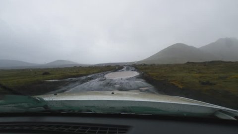 View from a car driving on a muddy road with potholes in Iceland.