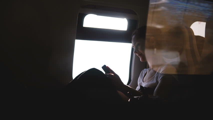 Beautiful European girl smiling happily, using smartphone social network app and looking around on train window seat. Royalty-Free Stock Footage #1014894415