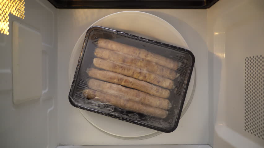 Top view defrosting sausages in microwave. Plastic container with breakfast sausage spinning in microwave. Royalty-Free Stock Footage #1014899872