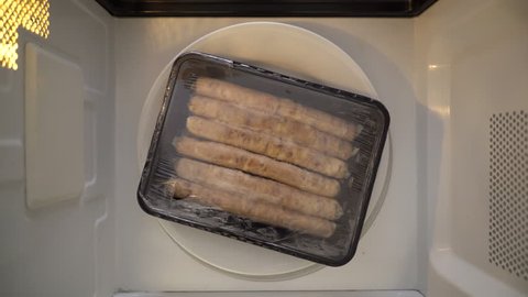 Top view defrosting sausages in microwave. Plastic container with breakfast sausage spinning in microwave.