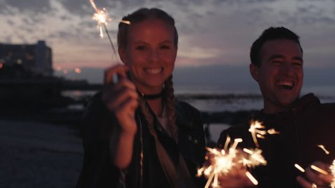 portrait of friends celebrating new years eve holding sparklers smiling happy cheerful enjoying beach party real people series