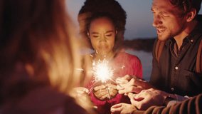 young blonde woman taking photo video of friends holding sparklers celebrating new years eve using smartphone enjoying beach party at sunset fun excitement
