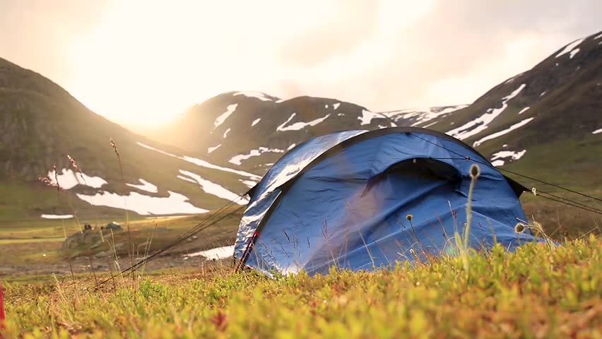 Tent on grass in front of a mountin with snow during sunset. Located in northern Sweden.