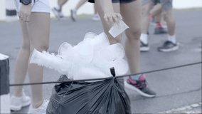 Group of runners on marathon near point of refreshment. They throwing a glass of plastic into a black garbage bag. video 4K 