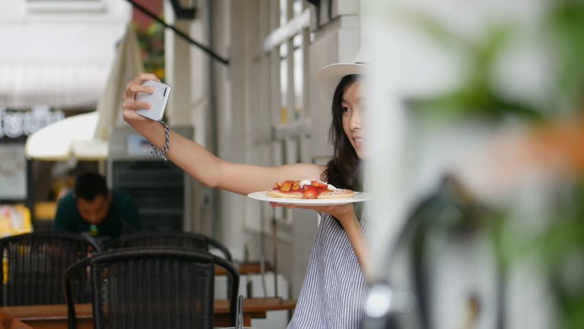 Beautiful asian woman taking selfies on a smartphone. Young asian girl take photo with pancake at cafe shop. Royalty-Free Stock Footage #1014913588