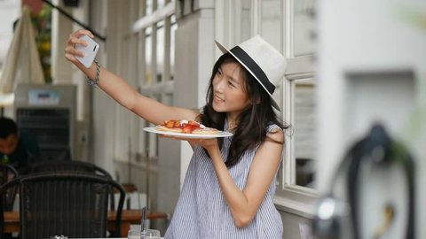 Beautiful asian woman taking selfies on a smartphone. Young asian girl take photo with pancake at cafe shop.