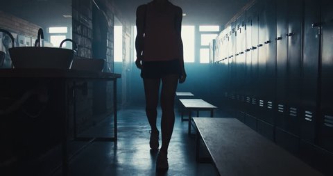 DOLLY IN Caucasian female athlete preparing for a workout in a gym locker room, tying shoelaces before training session. 4K UHD 60 FPS SLOW MOTION