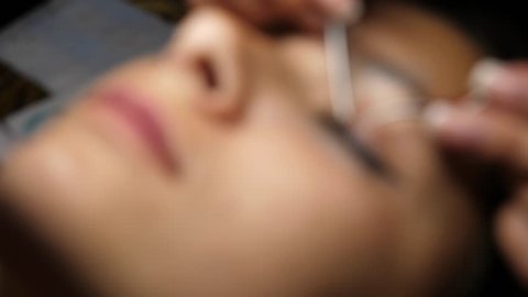 Woman eye with long eyelashes. Eyelash extension. transition from blurred away to focus. Gluing artificial eyelashes with tweezers. A woman lies under a lamp on a cosmetic procedure. top view.