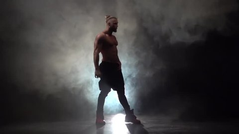 Pumped up guy dances a sexy dance. Black smoke background. Slow motion