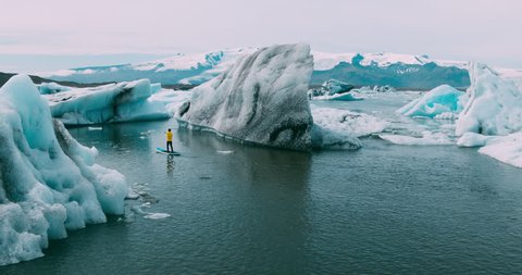 Aerial view of stand up paddle boarder paddling in glacier lake with giant icebergs in Iceland
