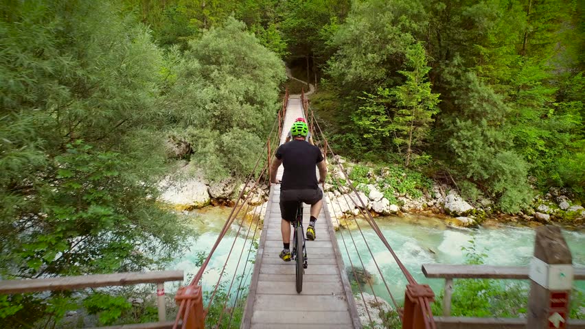 Aerial view of a man on a bicycle crossing wooden bridge at the Soca River, Slovenia.