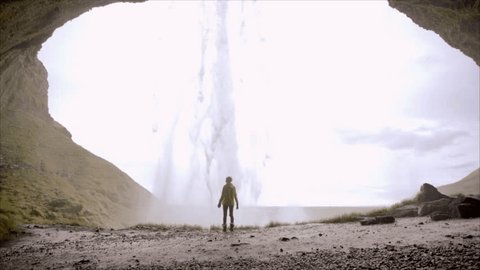 Young woman arms outstretched behind spectacular waterfall in Iceland. Slow motion shot of young woman outstretching arms by majestic waterfall. Success and achievement concept : film stockowy