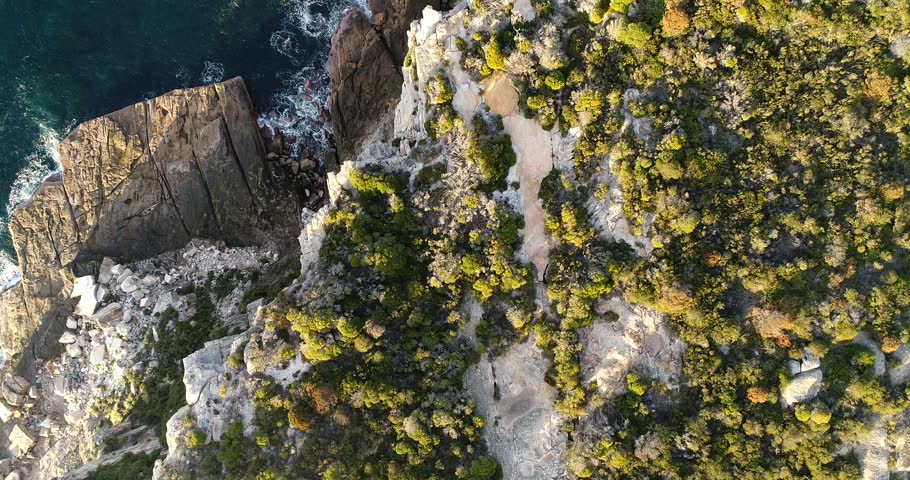 Endless waves hitting sandstone cliffs of North Head from surface and ground level lifting view up to distant Sydney city CBD skyline.

