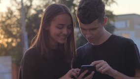 Couple sharing media in a smart phone in a park with buildings in the background
