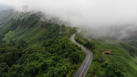 Aerial top view of sky road over top of mountain with fog and green jungle after raining in morning, Pua, Nan, Thailand. The transportation road across mountain. Shot from drone.
