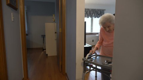 A senior woman walking down a hallway at a care home with a walker