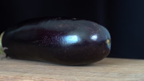 Hands of a chef cutting a large ripe eggplant in a kitchen with knife on wooden board, close up 