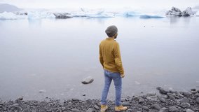 Young man arms outstretched at glacier lagoon in Iceland enjoying freedom in nature. Cold weather travel fun arms outstretched adventure concept 4K