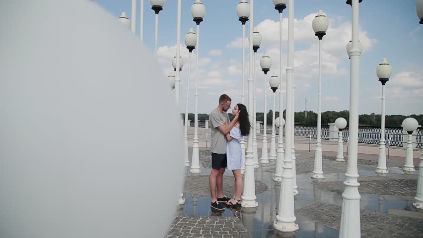 A loving couple hugs and kisses on the embankment near the street lamps.