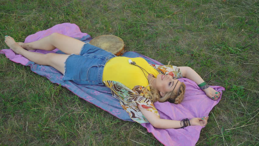 young blond hippie woman lies in the park at sunset. Warm summer day and soft backlight. the woman lies on the green grass.