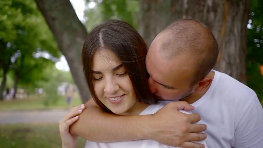man is embracing his girlfriend tenderly from back, stroking her long dark hair and kissing neck