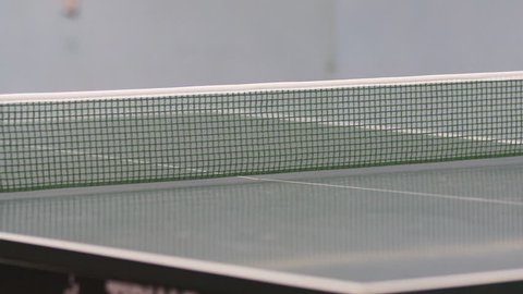 We can see a white ping pong ball travelling from one side of the table to another. Mens are playing table tennis.