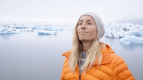Young woman arms outstretched at glacier lagoon in Iceland enjoying freedom in nature embracing life and vitality. People travel discovery adventure success concept. 4K resolution