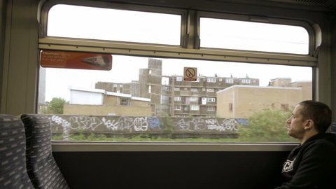 LONDON - APRIL 30, 2018: man on moving train looking out window, graffiti in ghetto in LDN, ENG, UK. The capital of England and the UK is a 21st-century city with history dating back to Roman times.