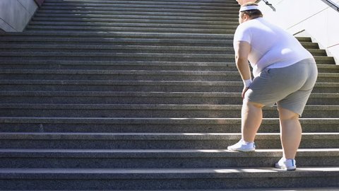 Obese man climbing stairs, overweight causes pain in joints, varicose veins