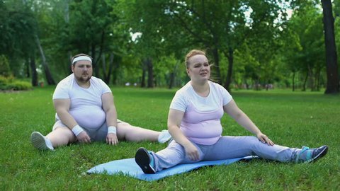 Fat couple having workouts in park together, beginners in weight loss program
