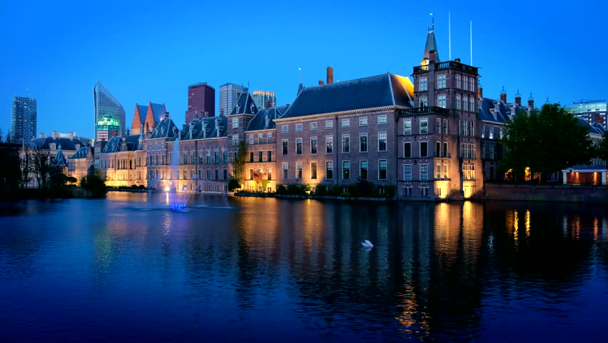 View of the Binnenhof House of Parliament and the Hofvijver lake with downtown skyscrapers in background illuminated in night. The Hague, Netherlands