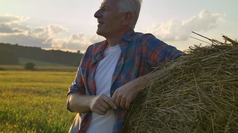 Young man greeting old farmer and shaking his hand, going away on straw field, beautiful landscape during sunset in background