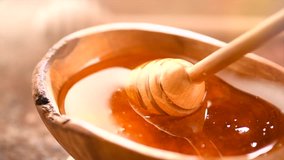 Honey dripping, pouring from honey dipper in wooden bowl.  Close-up. Healthy organic Thick honey dipping from the wooden honey spoon, closeup. 4K UHD video footage. Slow motion
