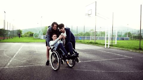 A boy in wheelchair with smartphone and teenager friends taking selfie.
