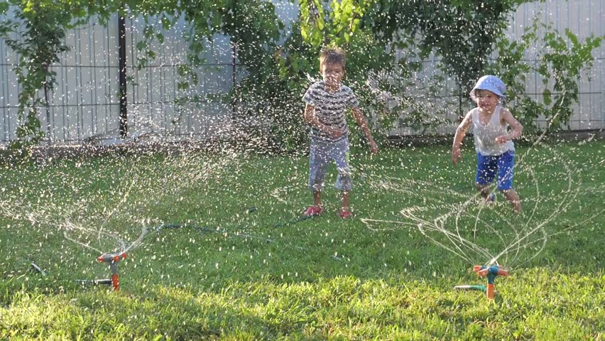 Boys playing an exciting game outdoor. Watering system. Children having fun while watering play yard.