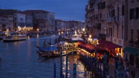 Blurred background of city lights and people walking along the Grand canal in evening. Colorful Venetian buildings with arched windows and balconies along the channel. 4k