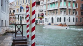 Defocused shot of red and white striped poles on Grand Canal while boat rides past. Exterior scene of old Venetian buildings and sea channel in Italy. 4k