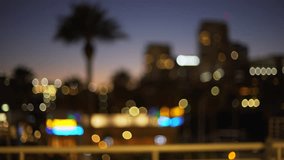 Blurry background plate of downtown city skyline in California city at night. Out of focus Video backdrop of urban area with palm tree in the evening for green screen compositing. 4k