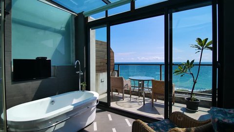 Beautiful Sea view Bathroom Interior Track Shot. Balcony with beautiful blue sky and sea view with chairs and table outside a luxury bathroom with glass ceiling. 